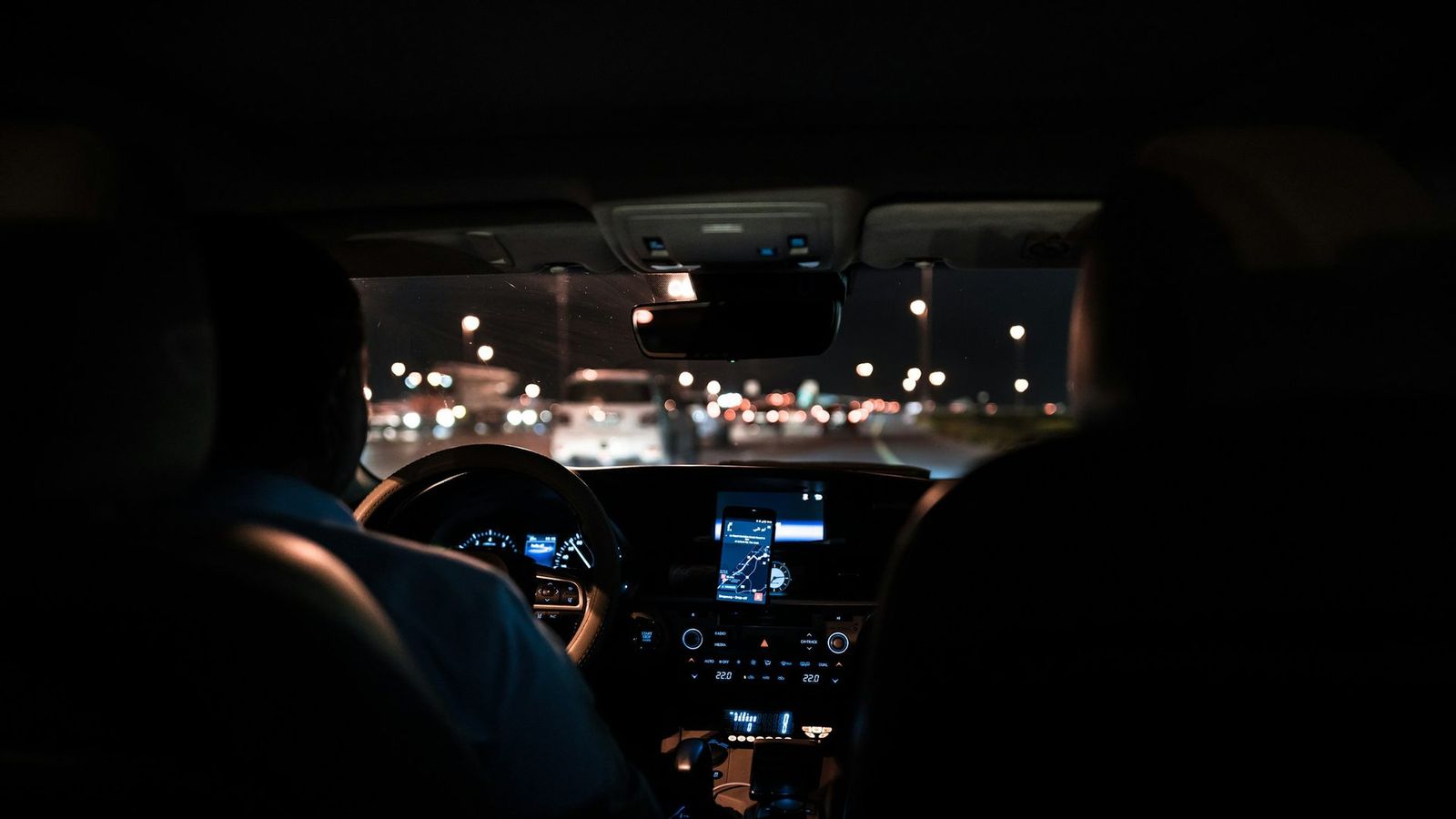 View from the rear seat of a car at night, the driver silhouetted against city lights